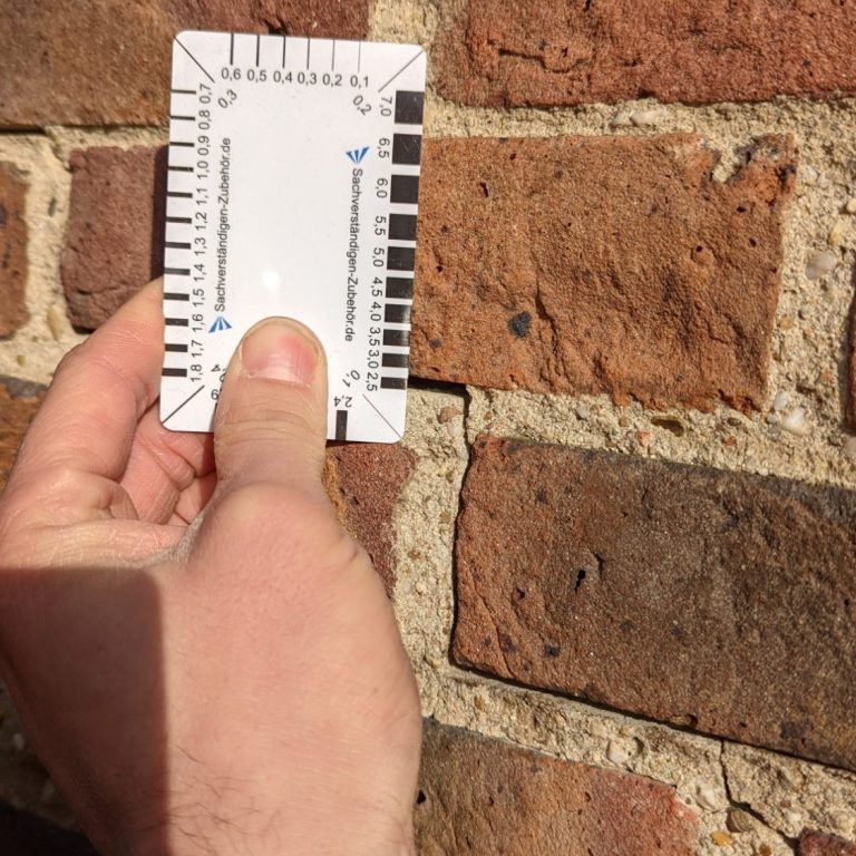 Eine Hand hält eine Karte vor einer roten Backsteinmauer.