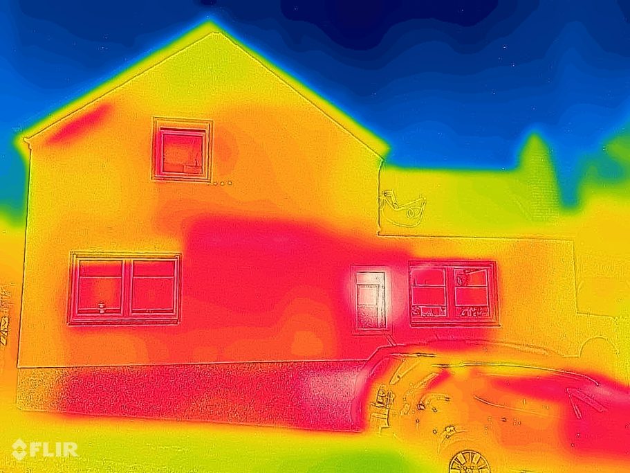 Thermografische Aufnahme eines Hauses, die Temperaturverteilung zeigt. Warme Bereiche erscheinen in Rot und Gelb um Fenster und Türen.