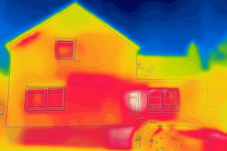 Thermografische Aufnahme eines Hauses, die Temperaturunterschiede zeigt. Die Farben variieren von blau und grün bei kühleren Bereichen zu rot und gelb bei wärmeren Stellen, vor allem um Fenster und Türen.